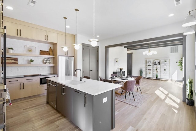 kitchen featuring decorative light fixtures, sink, a kitchen island with sink, stainless steel appliances, and light hardwood / wood-style flooring