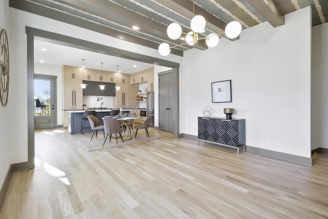 dining room with an inviting chandelier, beam ceiling, sink, and light hardwood / wood-style flooring