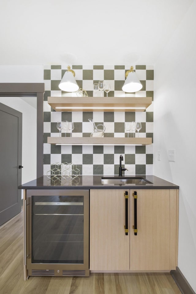 bar featuring light brown cabinetry, sink, tasteful backsplash, light wood-type flooring, and beverage cooler