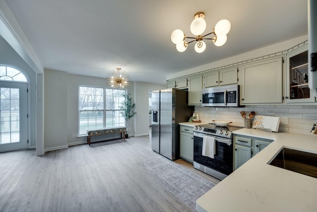 kitchen featuring sink, decorative backsplash, appliances with stainless steel finishes, a notable chandelier, and light hardwood / wood-style floors