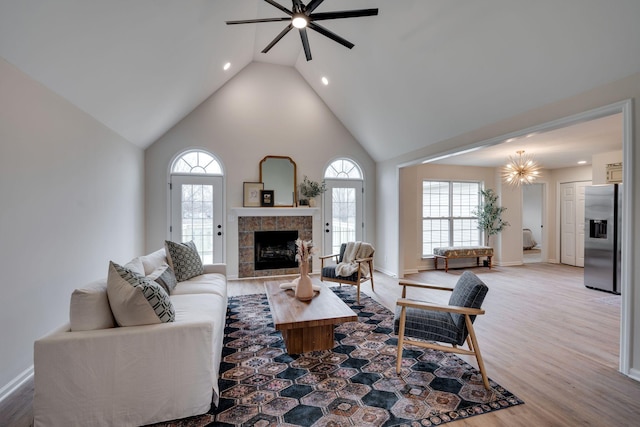 living room featuring hardwood / wood-style floors, high vaulted ceiling, ceiling fan, and a tiled fireplace