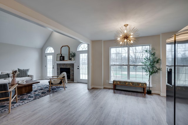 living room with a fireplace, wood-type flooring, vaulted ceiling, and an inviting chandelier