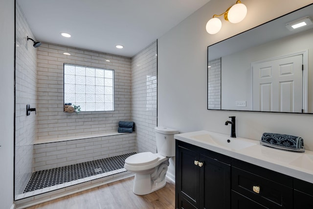 bathroom with hardwood / wood-style floors, toilet, a tile shower, and vanity