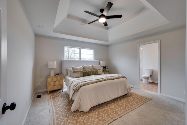 bedroom with ceiling fan, light colored carpet, connected bathroom, and a tray ceiling