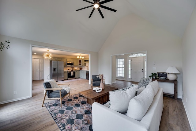 living room featuring ceiling fan with notable chandelier, light hardwood / wood-style floors, high vaulted ceiling, and sink