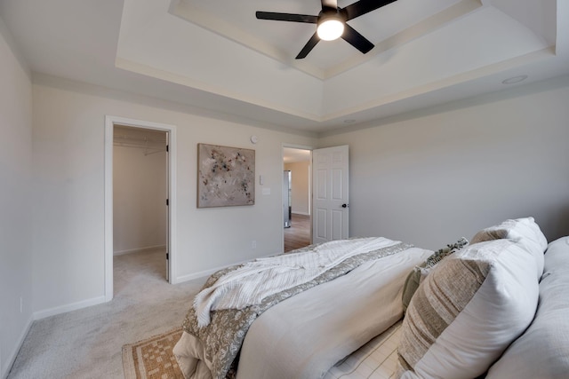 carpeted bedroom with a tray ceiling, a spacious closet, a closet, and ceiling fan