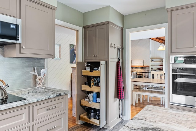 kitchen with light stone countertops, tasteful backsplash, gray cabinetry, stainless steel appliances, and light hardwood / wood-style flooring