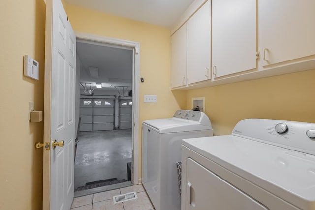 clothes washing area with cabinets, light tile patterned floors, and washing machine and dryer