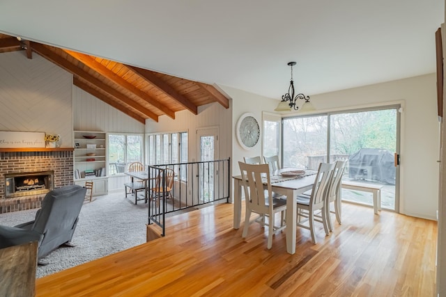 dining space featuring lofted ceiling with beams, light wood-type flooring, a fireplace, a notable chandelier, and wood ceiling