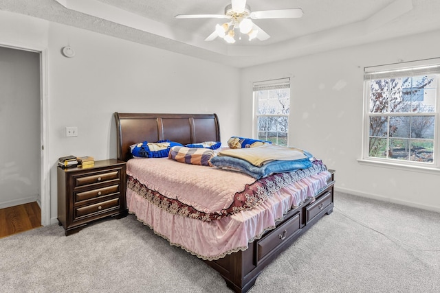 bedroom featuring a raised ceiling, ceiling fan, and light colored carpet