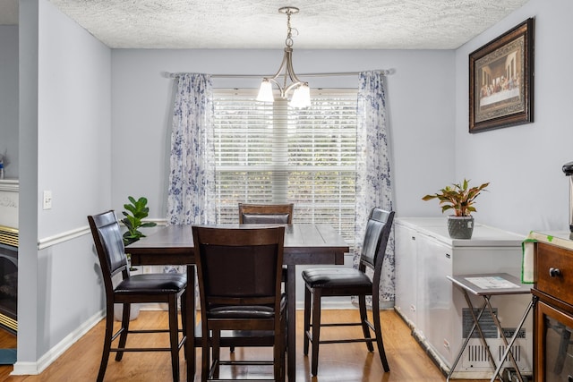 dining room with light hardwood / wood-style flooring, a textured ceiling, and an inviting chandelier