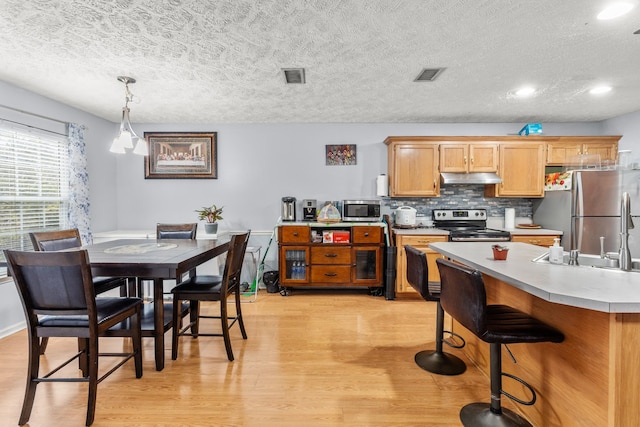 kitchen featuring sink, a textured ceiling, decorative light fixtures, appliances with stainless steel finishes, and light wood-type flooring