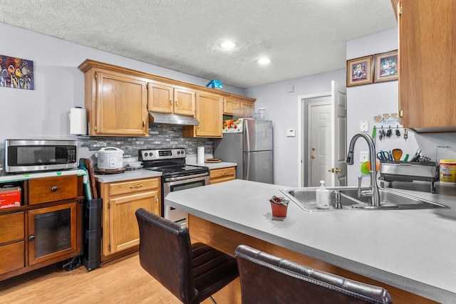 kitchen featuring sink, stainless steel appliances, tasteful backsplash, light hardwood / wood-style floors, and a textured ceiling