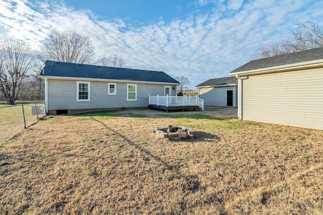 rear view of property featuring a lawn, a wooden deck, and a fire pit