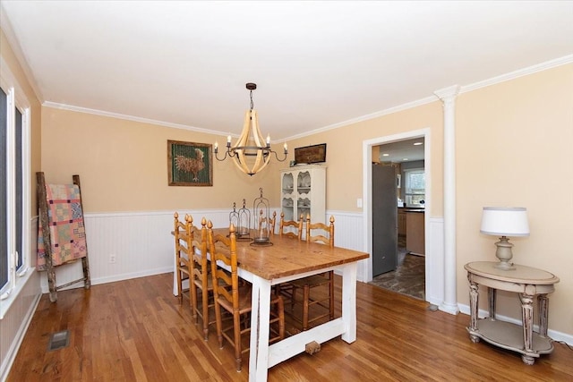 dining space featuring a chandelier, wood-type flooring, ornamental molding, and decorative columns