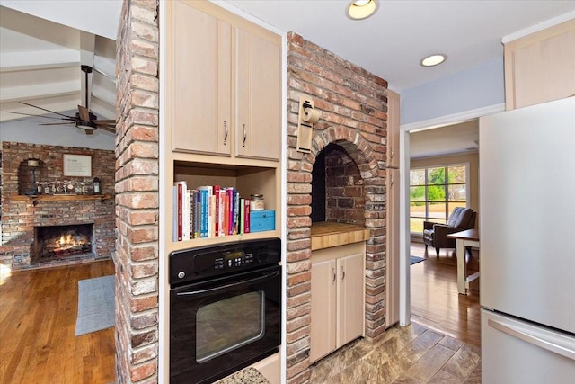 kitchen with light hardwood / wood-style flooring, beamed ceiling, white refrigerator, black oven, and a fireplace