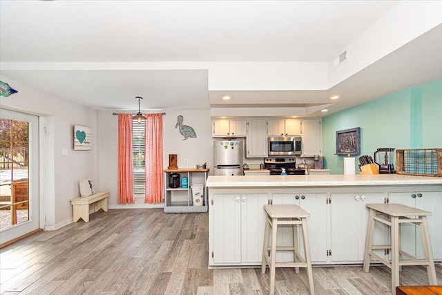 kitchen with a kitchen breakfast bar, light hardwood / wood-style floors, decorative light fixtures, and appliances with stainless steel finishes