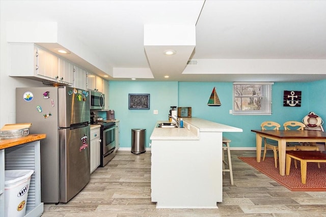 kitchen with kitchen peninsula, a kitchen breakfast bar, stainless steel appliances, light hardwood / wood-style floors, and white cabinetry