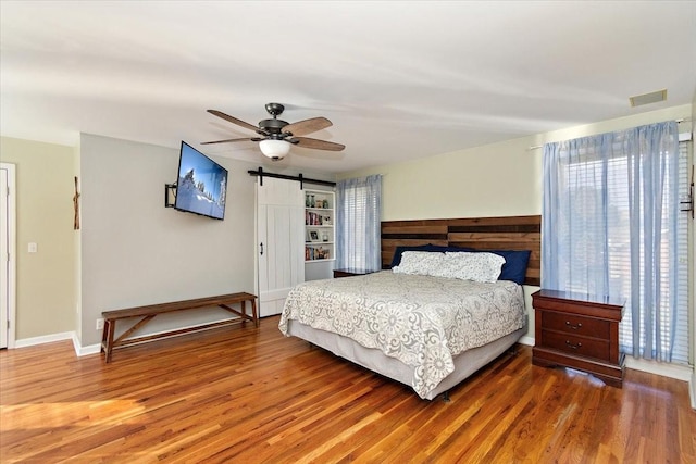 bedroom featuring wood-type flooring, a barn door, and ceiling fan