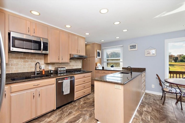 kitchen featuring kitchen peninsula, light brown cabinetry, dark stone counters, stainless steel appliances, and sink