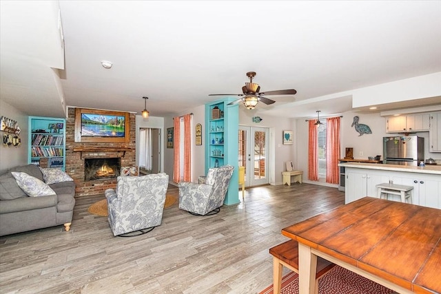 living room with ceiling fan, light wood-type flooring, french doors, and a brick fireplace