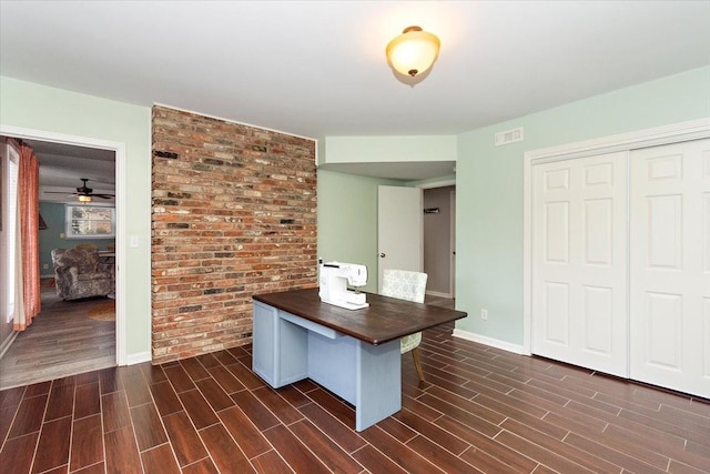 unfurnished office with dark hardwood / wood-style flooring, ceiling fan, and brick wall