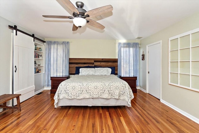 bedroom with hardwood / wood-style flooring, ceiling fan, and a barn door