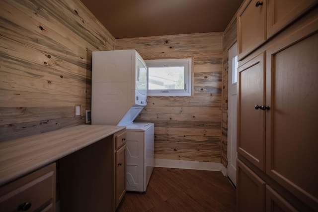 clothes washing area featuring dark wood-type flooring, cabinets, stacked washing maching and dryer, and wood walls