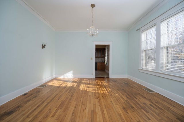 empty room featuring crown molding, wood-type flooring, and a notable chandelier