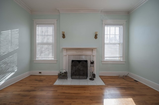 unfurnished living room featuring crown molding, wood-type flooring, a tile fireplace, and plenty of natural light