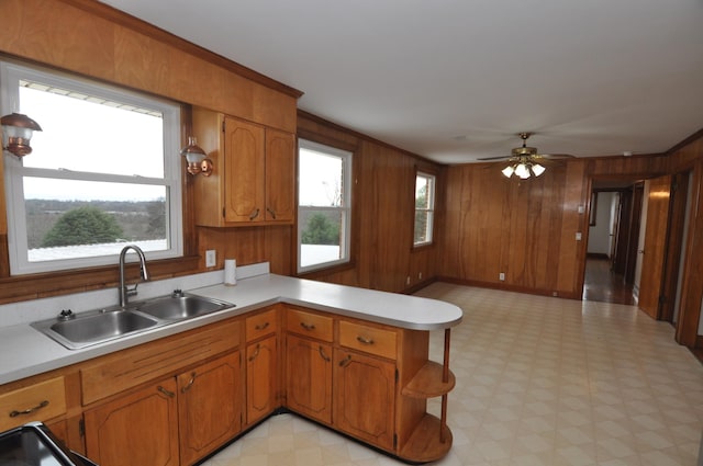 kitchen with ceiling fan, wooden walls, kitchen peninsula, and sink