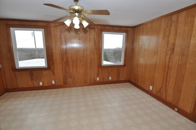 unfurnished room featuring plenty of natural light, ceiling fan, and wood walls