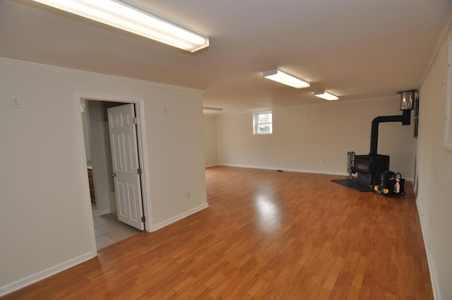 basement with ornamental molding, a wood stove, and light hardwood / wood-style flooring