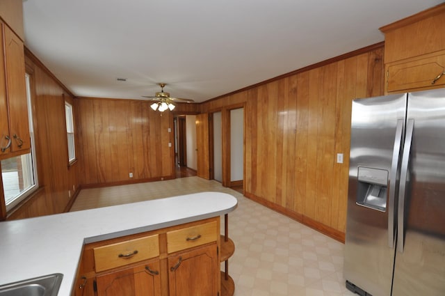 kitchen featuring wooden walls, ornamental molding, ceiling fan, and stainless steel refrigerator with ice dispenser