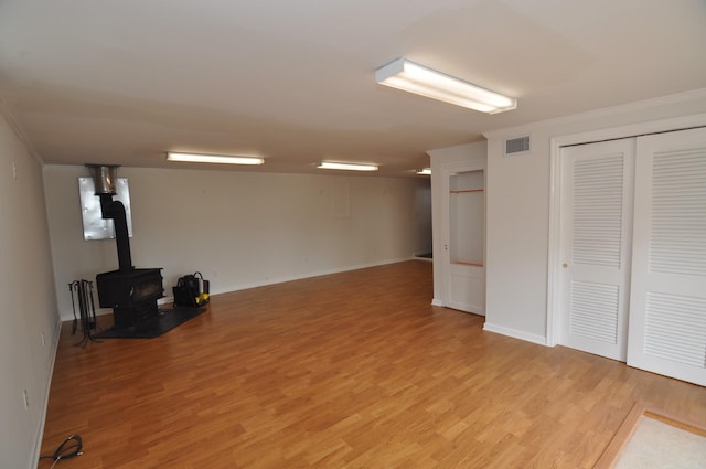 basement featuring ornamental molding, a wood stove, and light hardwood / wood-style floors