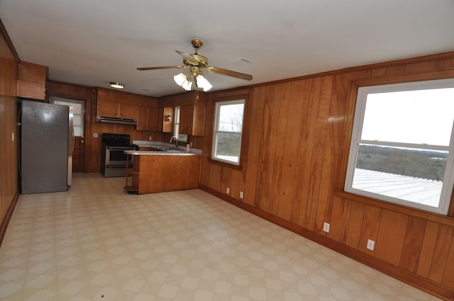 kitchen with sink, appliances with stainless steel finishes, wooden walls, kitchen peninsula, and ceiling fan