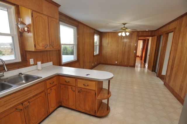 kitchen with crown molding, kitchen peninsula, sink, and wood walls