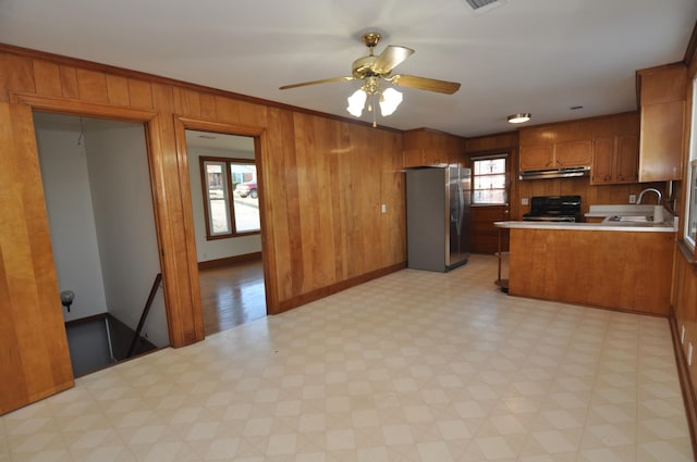 kitchen with sink, stainless steel refrigerator, electric range, kitchen peninsula, and wood walls