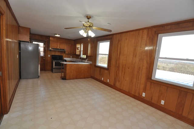 kitchen featuring sink, crown molding, appliances with stainless steel finishes, wooden walls, and kitchen peninsula