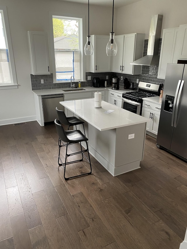 kitchen with sink, wall chimney range hood, stainless steel appliances, a center island, and decorative light fixtures