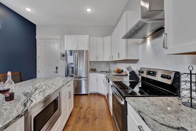 kitchen with appliances with stainless steel finishes, sink, white cabinetry, and wall chimney range hood