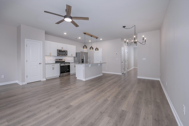 kitchen with decorative light fixtures, appliances with stainless steel finishes, a kitchen island, ceiling fan with notable chandelier, and white cabinets