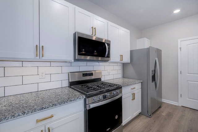 kitchen with appliances with stainless steel finishes, white cabinets, decorative backsplash, light stone counters, and light hardwood / wood-style flooring