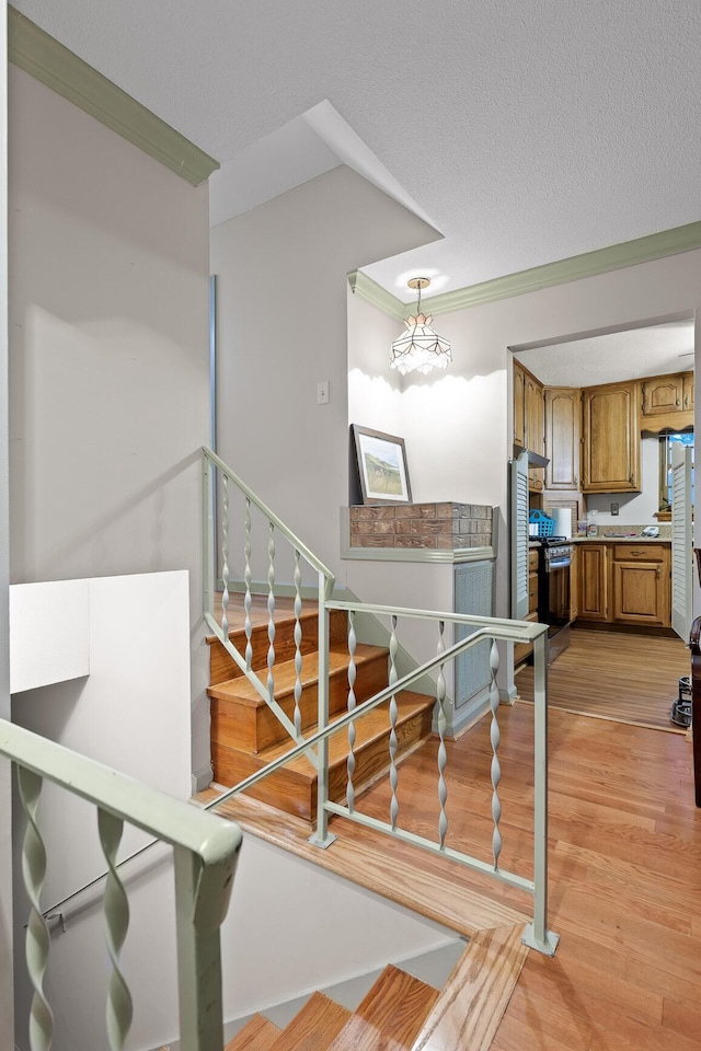 stairway featuring hardwood / wood-style floors, a textured ceiling, and ornamental molding