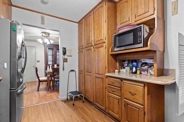 kitchen with appliances with stainless steel finishes, light wood-type flooring, a textured ceiling, ceiling fan, and crown molding