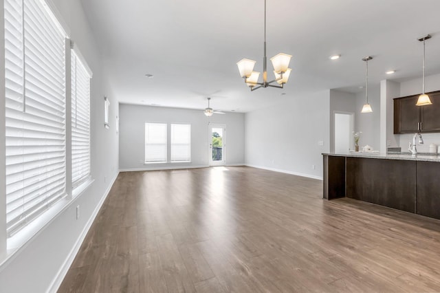 unfurnished living room featuring sink, ceiling fan with notable chandelier, and hardwood / wood-style flooring