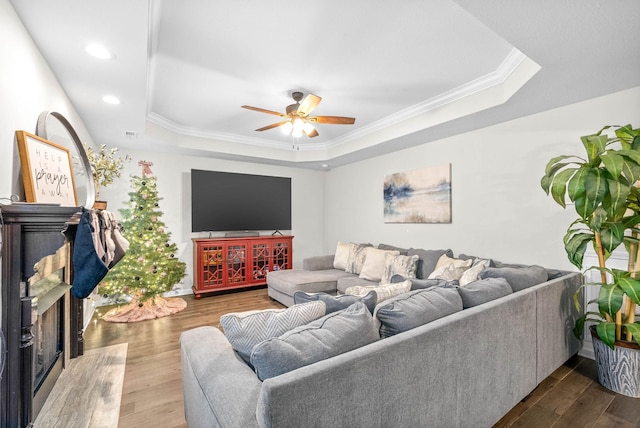 living room featuring dark hardwood / wood-style flooring, a tray ceiling, ceiling fan, and ornamental molding