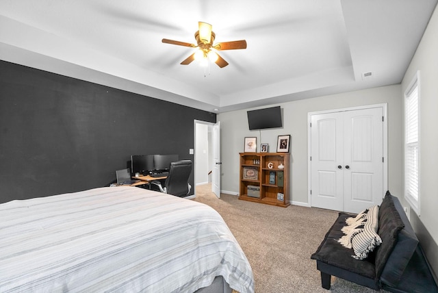 carpeted bedroom featuring a tray ceiling, ceiling fan, and a closet