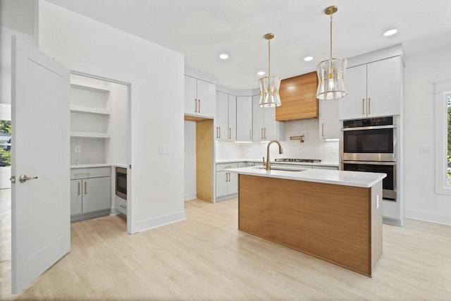 kitchen featuring stainless steel appliances, white cabinetry, a center island with sink, and light hardwood / wood-style floors