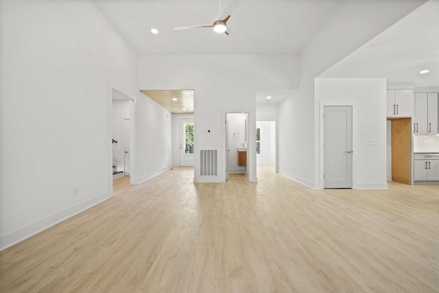 unfurnished living room with a towering ceiling, light wood-type flooring, and ceiling fan